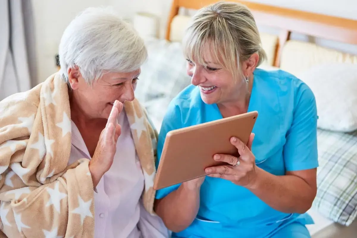 A carer sitting with a resident, sharing something on a tablet