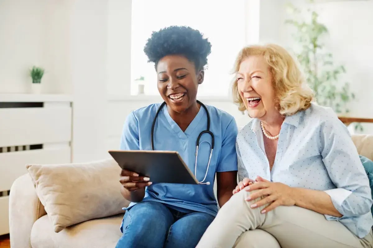 A nurse and a resident laughing together over a tablet