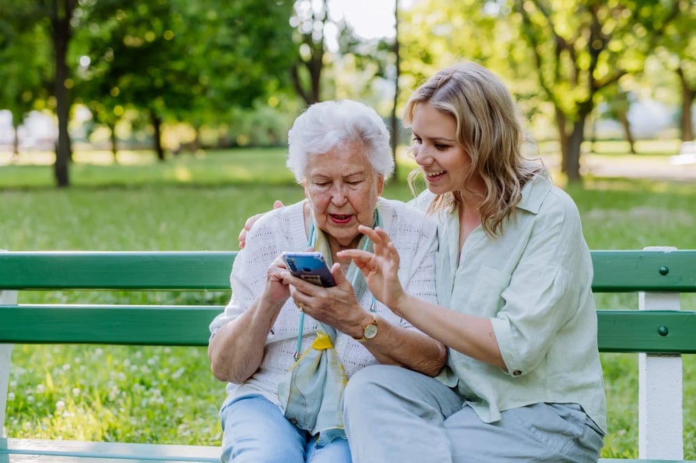 elderly woman looking at phone with carer