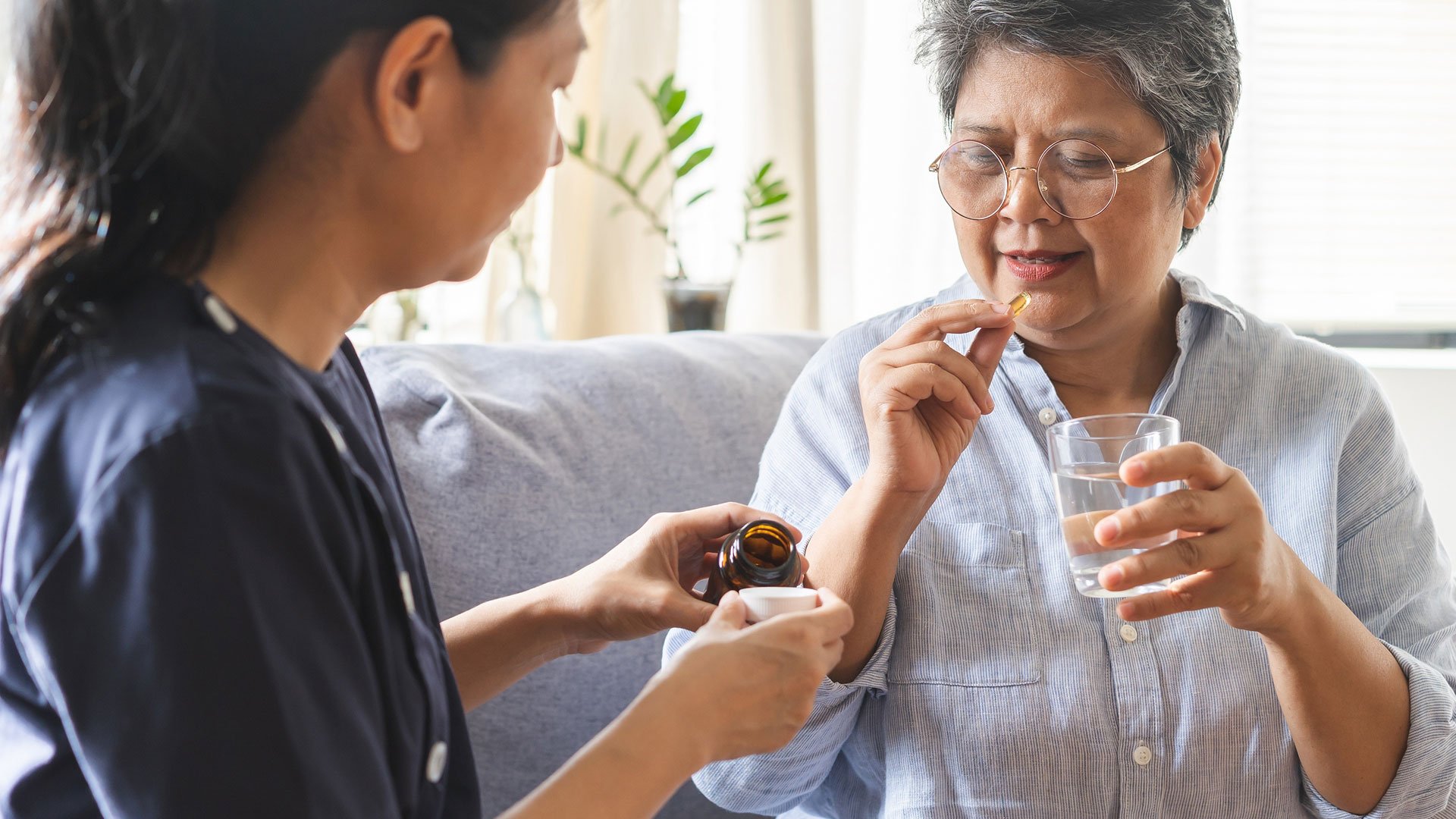 Resident woman take a pill with a glass of water, helped by a carer