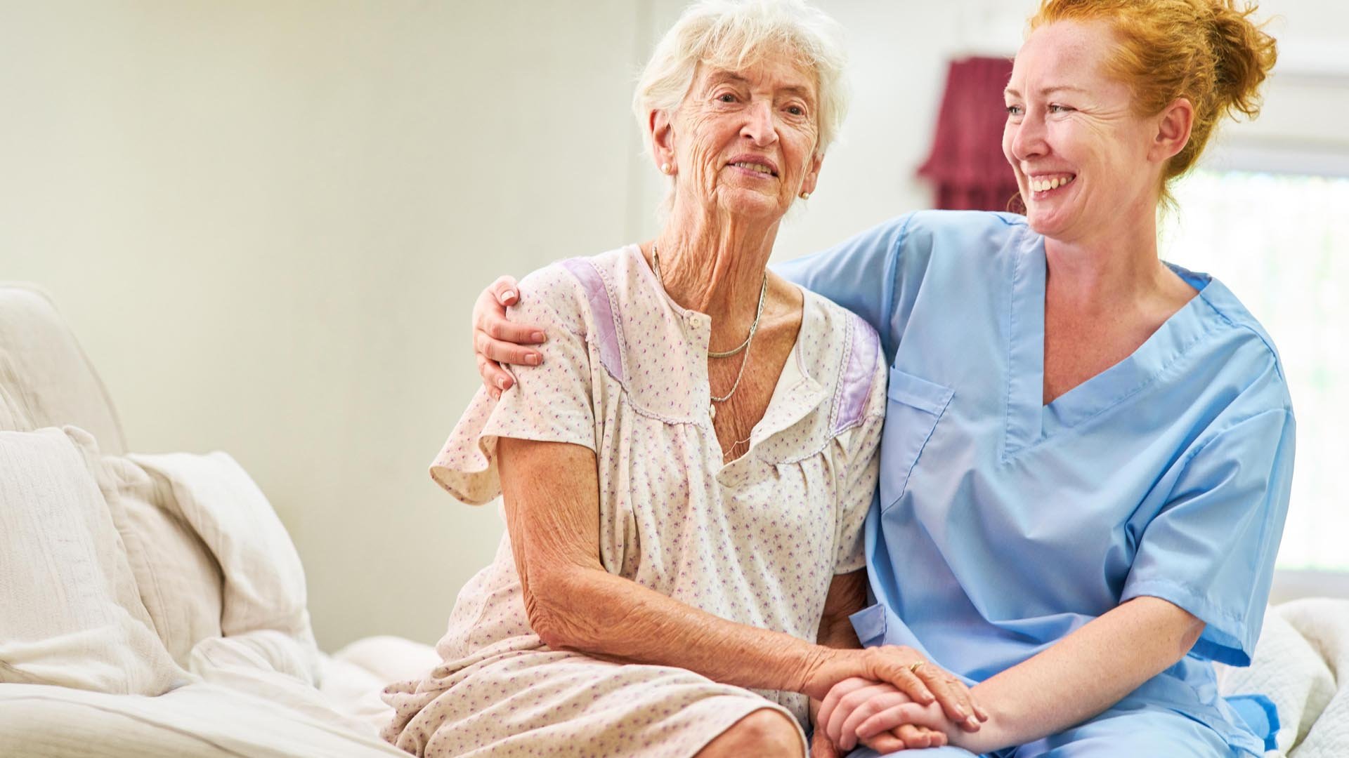 Carer wearing scrubs sits with a resident in a nightgown
