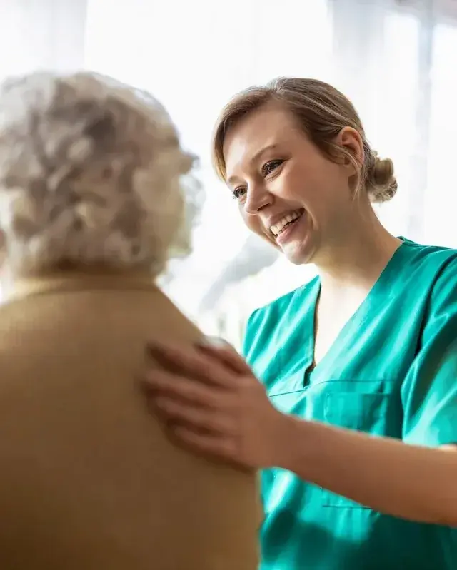 A care team member smiling with a resident, resting a hand on her shoulder.